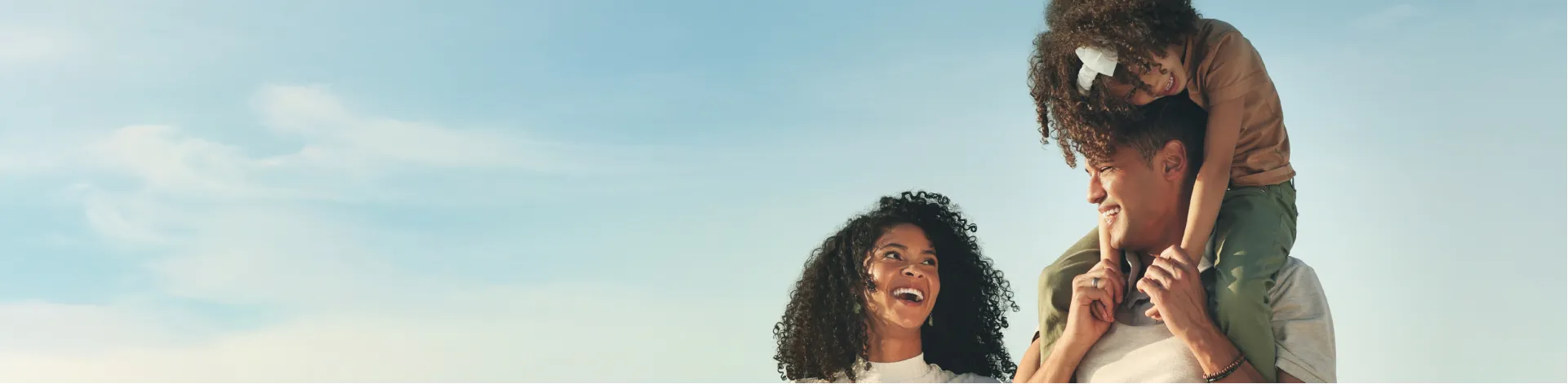 Mulher sorrindo para o marido enquanto ele carrega a filha nos ombros, mostrando o cuidado da Horiens com funcionários e famílias.